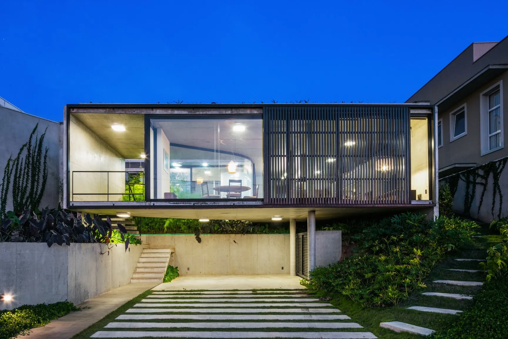 Casa LEnS ao anoitecer, com o volume de vidro suspenso sobre a garagem aberta